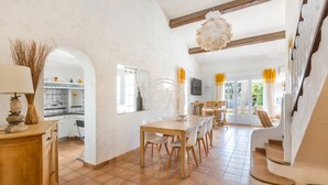A spacious dining area with a wooden table and chairs, a kitchen in the background, and a staircase leading to another level. - Charming Provencal house with swimming pool (Bormes-les-Mimosas)