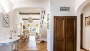 A spacious hallway with a wooden door, a dining area with tables and chairs, and a staircase leading to an upper level. - Charming Provencal house with swimming pool (Bormes-les-Mimosas)