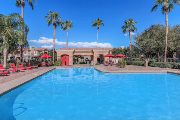 A swimming pool with red umbrellas, palm trees, and a building with a red door. - Vacation Worthy and great Location (Mesa)
