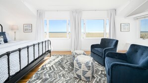 Ein Schlafzimmer mit Bett, zwei Stühlen, einem kleinen Tisch und Blick auf den Strand.