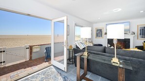 Ein Wohnzimmer mit einem großen Glasfenster, das auf einen Balkon mit Blick auf einen Strand führt.