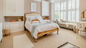 A bedroom with a large bed, a bedside table, a dresser, a vanity, and a window with shutters.