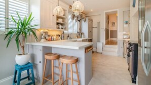 A modern kitchen with a central island, bar stools, pendant lighting, and a potted plant.