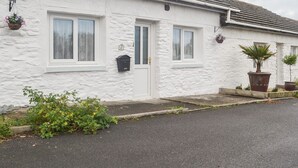 Une maison blanche à deux étages, avec un toit recouvert de tuiles grises, une porte d’entrée et deux fenêtres.