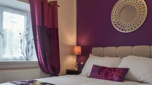 Une chambre à coucher avec un lit, des rideaux violets, une lampe de chevet et un miroir décoratif accroché au mur.
