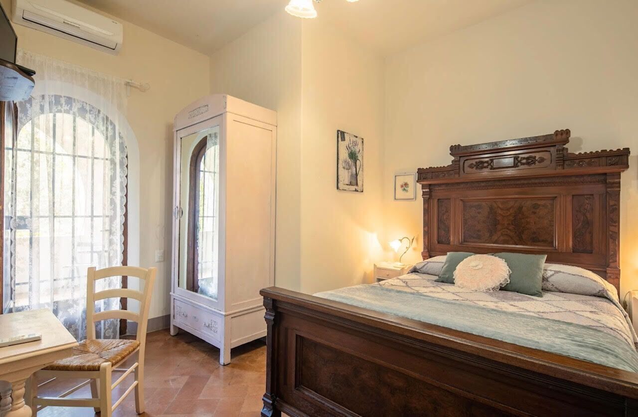 A bedroom with a wooden bed, a desk with a chair, a window with curtains, and an air conditioning unit.