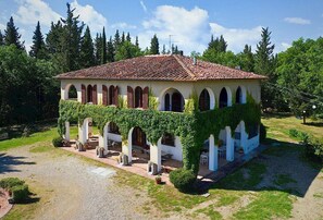 A villa with a tiled roof, arched windows, and a covered patio area with outdoor seating. - Splendid Chianti Tuscany Villa with Panoramic Pool ,Cypress Trees-Lined Drive (Montespertoli)
