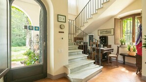 Trappeføjelse op til en etage, et spiseområde med bord og stole, samt en dør med udsigt over haven.