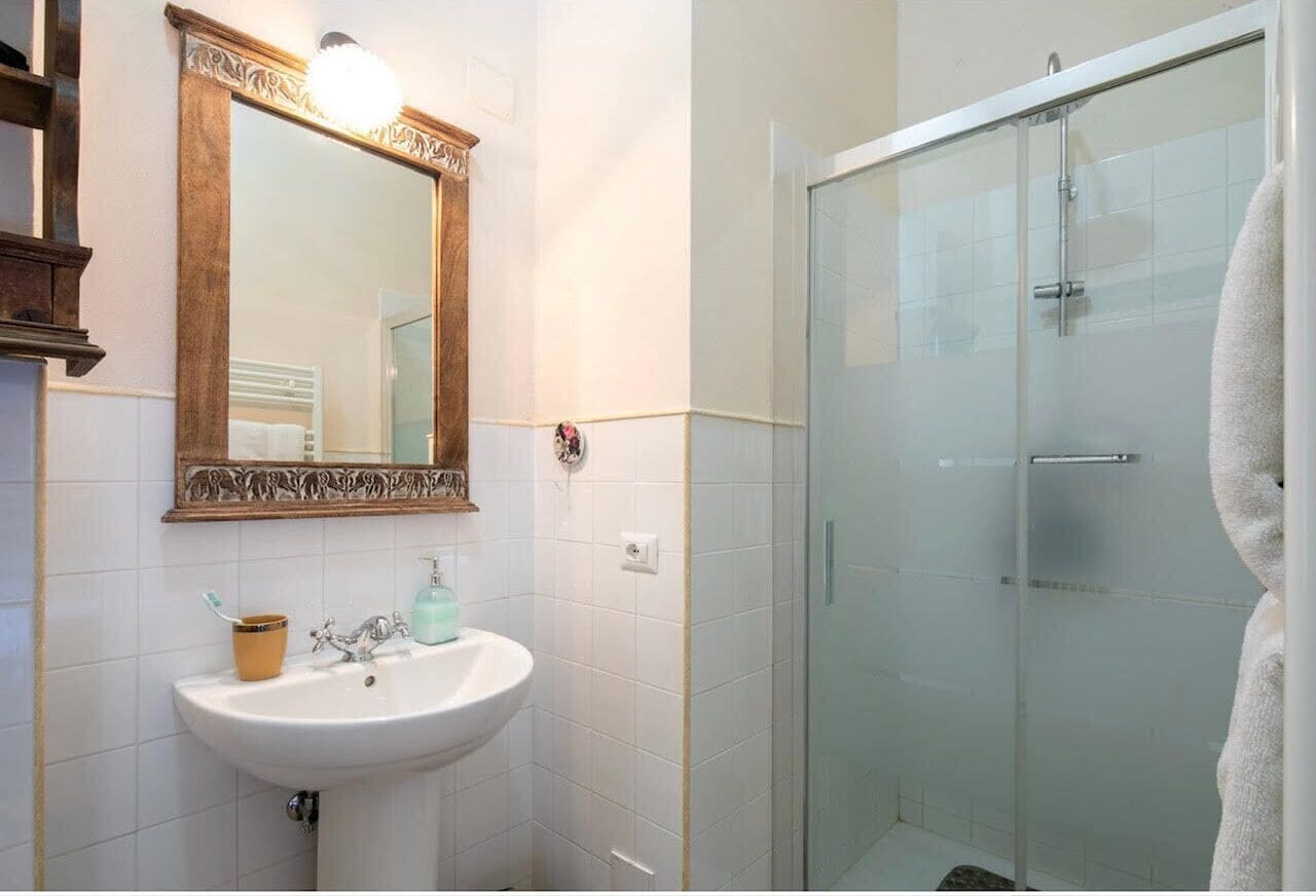 A bathroom with a white sink, a mirror with an ornate frame, and a glass shower enclosure.