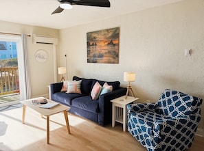 A living room with a dark blue sofa, a patterned armchair, a small table, and a painting on the wall.