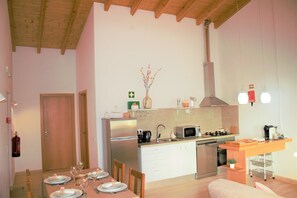 A modern kitchen with a dining area, featuring a wooden ceiling, stainless steel appliances, and a small island with a sink.