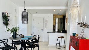 Une cuisine moderne avec un réfrigérateur en acier inoxydable, un coin repas comprenant une table ronde et des chaises noires, ainsi qu’un meuble rouge agrémenté d’objets décoratifs.