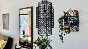 Un salon moderne agrémenté d’un luminaire suspendu aux formes géométriques, d’un miroir, d’une bibliothèque avec des objets décoratifs et d’une plante en pot.