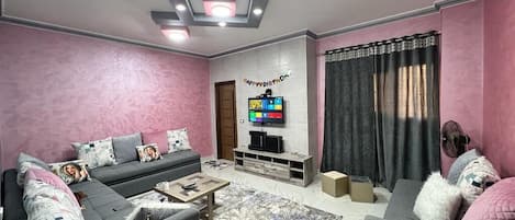 A living room with a sofa set, a coffee table, a flat-screen TV, and a patterned rug.