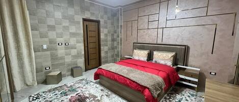 A bedroom with a bed, a headboard, a bedside table, and a patterned rug.