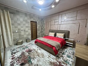 Un dormitorio con cama, cabecera, mesita de noche y alfombra estampada.