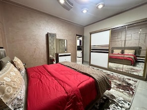 Quarto com cama, penteadeira, espelho e armário de portas deslizantes.