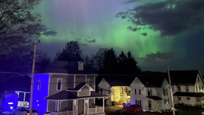 Un barrio residencial con casas bajo un cielo nocturno con la aurora boreal.