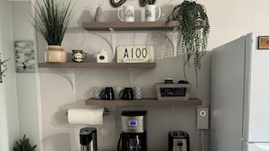 Una cocina decorada con temática de café, incluyendo un cartel que dice 'Coffee', una cafetera y tazas en estantes.
