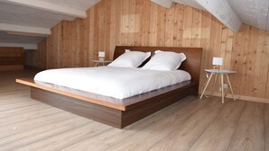 Een moderne slaapkamer met een houten lattenplafond, een groot bed met wit beddengoed en twee nachtkastjes met lampen.