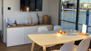 Ein moderner Essbereich mit einem großen Tisch, weißen Stühlen und Blick auf eine Marina mit Booten.