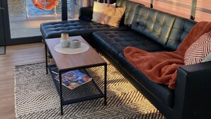 Ein modernes Wohnzimmer mit einer schwarzen Ledersofa, einem Holztisch und einem großen Fenster mit Blick auf das Wasser und den Steg.