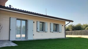 Une maison de plain-pied avec un toit plat, de grandes portes-fenêtres coulissantes et trois fenêtres équipées de volets.