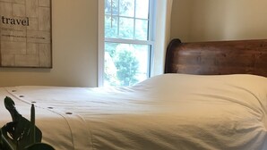 A single bed with a wooden headboard, white bedding, and a window with a view of greenery outside. - Shallow Lake Retreat (Shallow Lake)