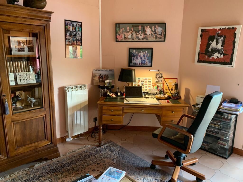 A home office with a wooden desk, a computer, a chair, a radiator, and a cabinet with decorative items.
