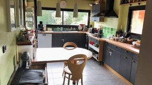 A kitchen with a central island, wooden chairs, a dining table, and a window with a view of greenery. - Family home at the foot of the Pyrenees (Clarac)
