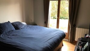 A bedroom with a large bed, a bedside table, and a view of the outdoors through a sliding door. - Family home at the foot of the Pyrenees (Clarac)
