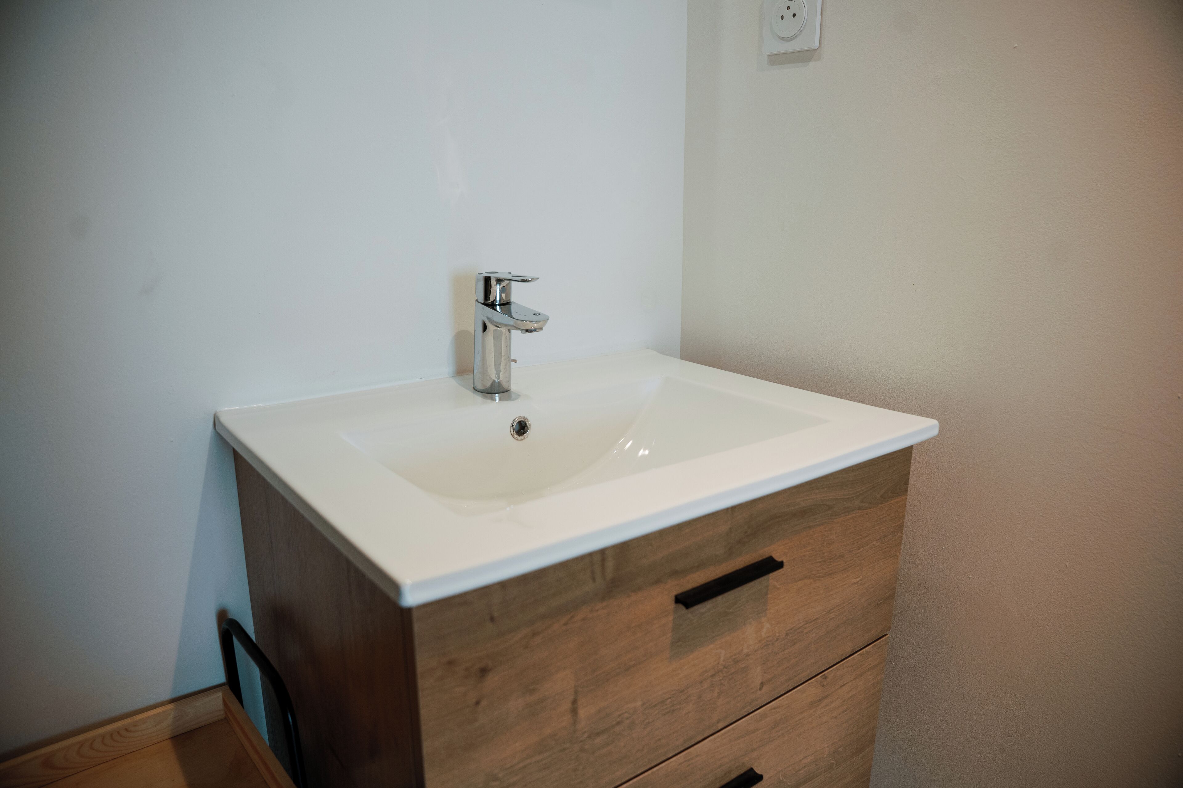 A bathroom with a white sink, wooden cabinet, and a wall socket.