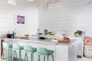Une cuisine moderne dotée d’un îlot central, de tabourets de bar, d’un luminaire suspendu et d’une œuvre d’art encadrée au mur.
