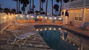 A pool area with lounge chairs, a small pool, and a building with string lights. - Halifax Riverfront Oasis - 8 Bedrooms with pool (Daytona Beach)