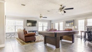 A spacious room with a pool table, a leather sofa, and a ceiling fan. - Halifax Riverfront Oasis - 8 Bedrooms with pool (Daytona Beach)