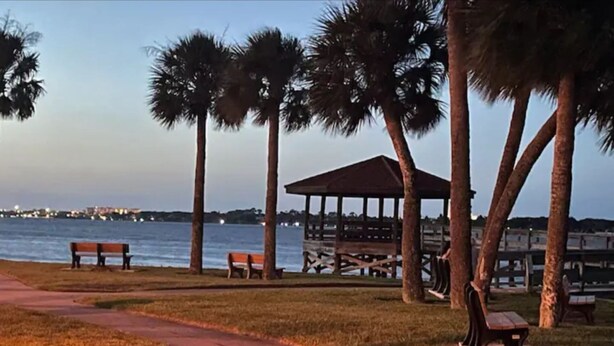 A park with a walking path, benches, palm trees, and a gazebo by the water. - Halifax Riverfront Oasis - 8 Bedrooms with pool (Daytona Beach)