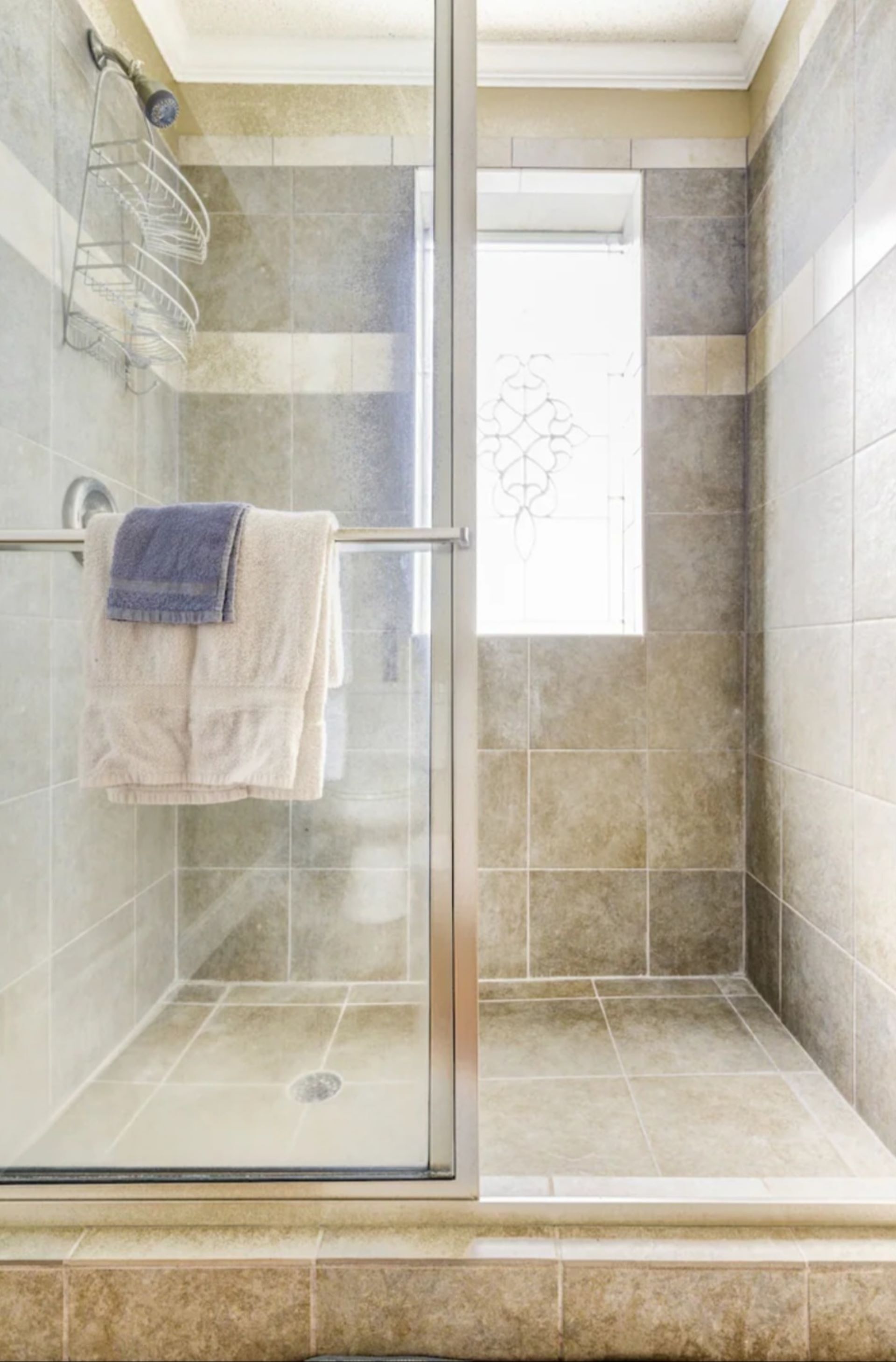 Um chuveiro com divisória de vidro, um porta-toalhas e uma janela decorativa.
