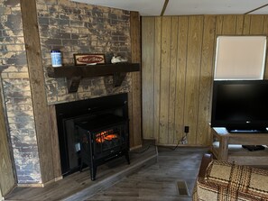 Un salon avec une cheminée en briques, un téléviseur fixé au mur et un plancher en bois.