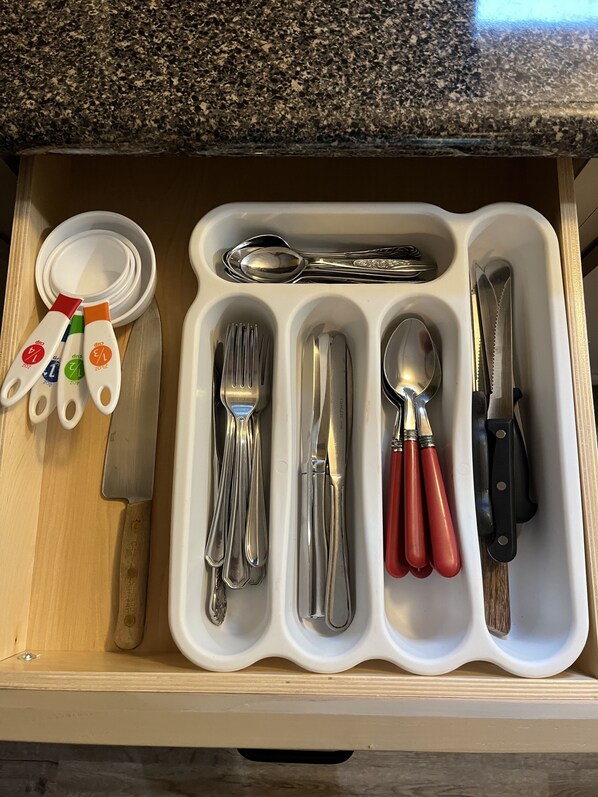 A drawer with a utensil organizer containing forks, spoons, knives, and a pair of scissors.