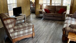 Un salon chaleureux avec des murs lambrissés, une grande fenêtre, un téléviseur et deux canapés à motifs.