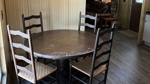 Un coin repas avec une table ronde et quatre chaises, des lambris en bois sur les murs, un lampadaire et une fenêtre avec des rideaux.