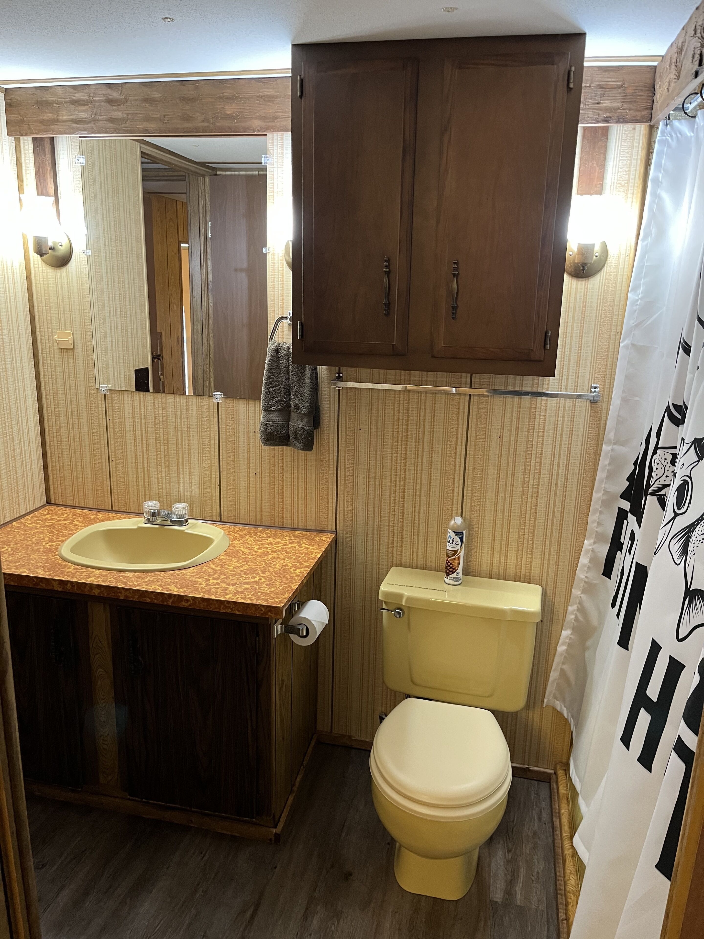 A compact bathroom with a wooden vanity, a toilet, and a shower curtain.