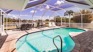 A swimming pool with a covered patio area, lounge chairs, and a view of the surrounding landscape.
