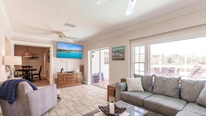 A spacious living room with a sofa, a glass coffee table, and a television mounted on the wall.