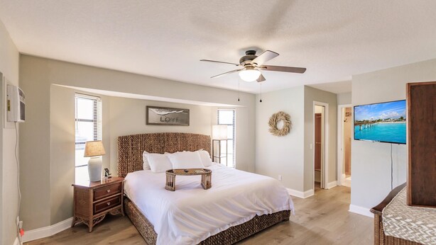 A bedroom with a large bed, a ceiling fan, a television, and a view of the ocean.