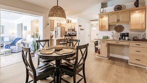 A modern kitchen with wooden cabinets, a dining area with a round table, and a hanging pendant light.