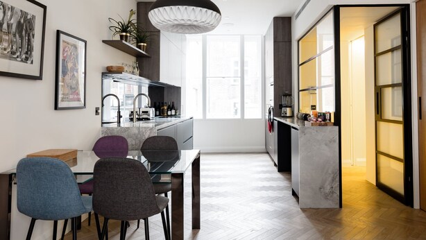 A modern kitchen with a dining area, featuring a herringbone wood floor, a glass dining table, and contemporary chairs. - Bright Spacious Modern One Bedroom Apartment (1) (London)