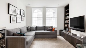 A modern living room with a sectional sofa, a flat-screen TV, and a herringbone-patterned floor. - Bright Spacious Modern One Bedroom Apartment (1) (London)