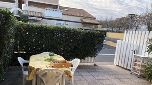 Une terrasse extérieure avec une table et des chaises, une clôture blanche et un bâtiment en arrière-plan.