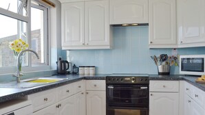 A kitchen with white cabinets, a black oven, a microwave, and a window with flowers. - 3 bedroom accommodation in Blakeney Hill, near Lydney, Forest of Dean (Blakeney Hill, near Lydney, Forest of Dean)